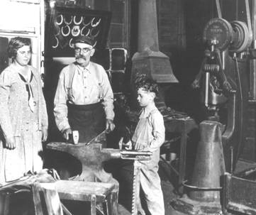 William Siebler inside his blacksmith shop with  youngest daughter, Mildred, and youngest son, Lee.   Aurora, Nebraska.  Circa 1932